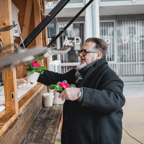 RawmanPictures - Sebastian Schiefermayr | Valentinsaktion Marchtrenk | Besucher kauft Blumen an Marktstand, Stadtleben, Outdoor-Fotografie, bunter Frühlingsmarkt.