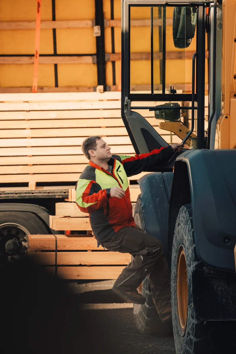 RawmanPictures - Sebastian Schiefermayr | Sägewerk Löberbauer | Mann auf Baustelle besteigt Bagger, Holz im Hintergrund, Bauwesen, Arbeitsfotografie.