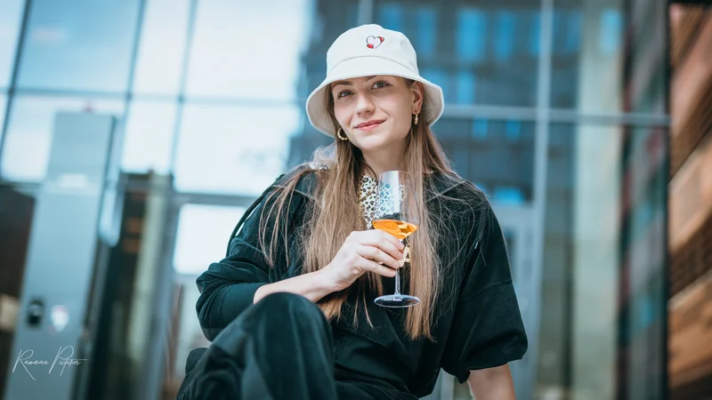 RawmanPictures - Sebastian Schiefermayr | Musikvideodreh "Flinz Asozial" | Moderne Lifestyle-Portraitfotografie, stilvolle Frau mit Drink vor urbanem Hintergrund.