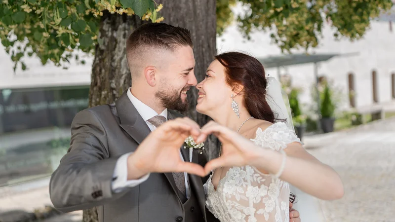 RawmanPictures - Sebastian Schiefermayr | Hochzeit Natalia & Jürgen | Romantische Hochzeitsfotografie im Freien, Brautpaar formt Herz im Vordergrund.