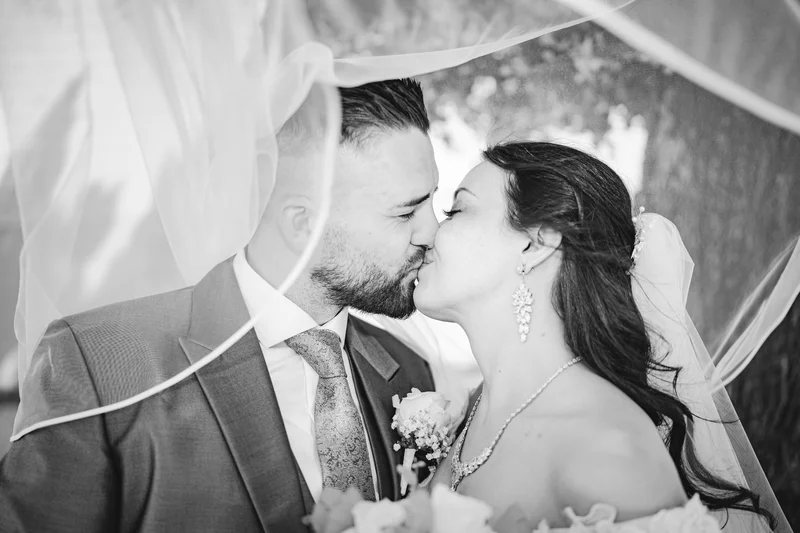 RawmanPictures - Sebastian Schiefermayr | Hochzeit Natalia & Jürgen | Hochzeitspaar Kuss unter Schleier, romantische Schwarz-Weiß-Fotografie, emotionsgeladenes Bild.