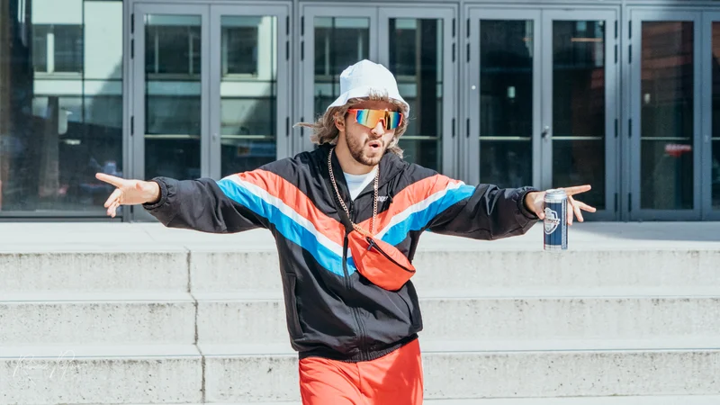 RawmanPictures - Sebastian Schiefermayr | Musikvideodreh "Flinz Asozial" | Lässige Modefotografie: Mann in bunter Sportkleidung und Sonnenbrille vor urbaner Kulisse.