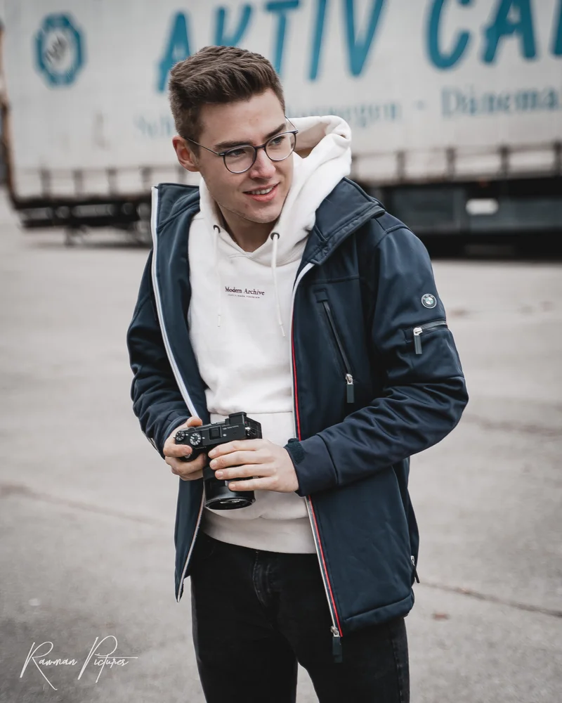 RawmanPictures - Sebastian Schiefermayr | Shooting Julian S. | Fotograf mit Kamera in urbaner Umgebung für moderne Porträtfotografie.
