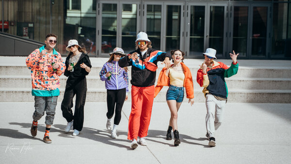 RawmanPictures - Sebastian Schiefermayr | Musikvideodreh "Flinz Asozial" | Gruppe junger Erwachsener in bunter Retro-Mode bei einem Outdoor-Fotoshooting.