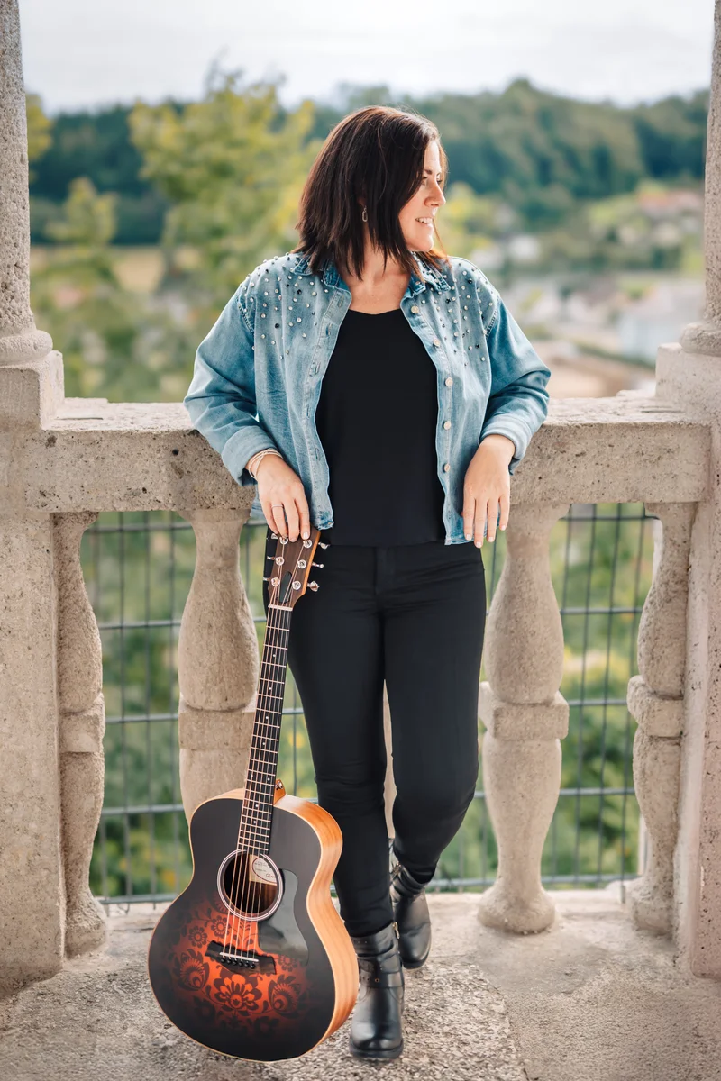 RawmanPictures - Sebastian Schiefermayr | Portraitshooting Tamara R. | Frau mit Gitarre auf Balkon, ländlicher Hintergrund. Outdoor-Portraitfotografie, Musik und Natur.