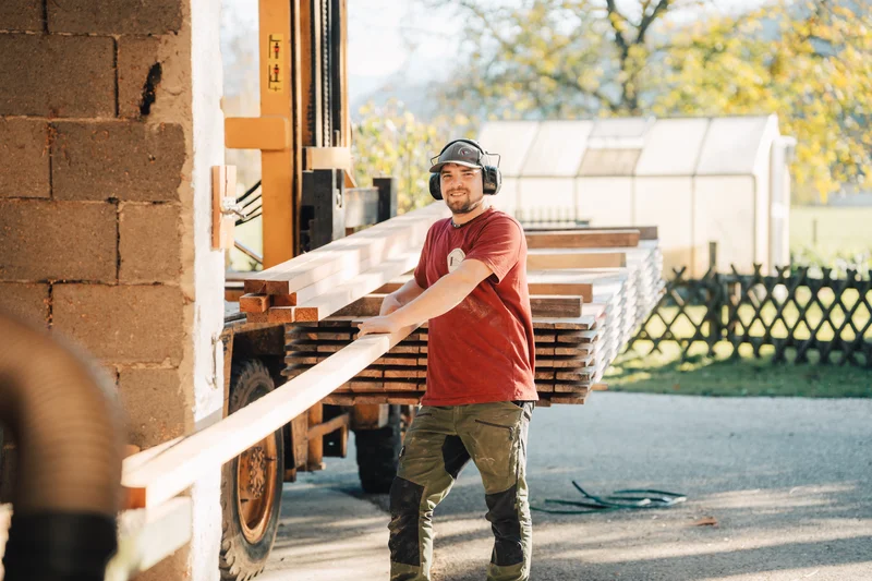 RawmanPictures - Sebastian Schiefermayr | Sägewerk Löberbauer | Arbeiter mit Holz in Sägewerk bei Sonnenlicht. Industriefotografie, Holzverarbeitung, Handwerk.