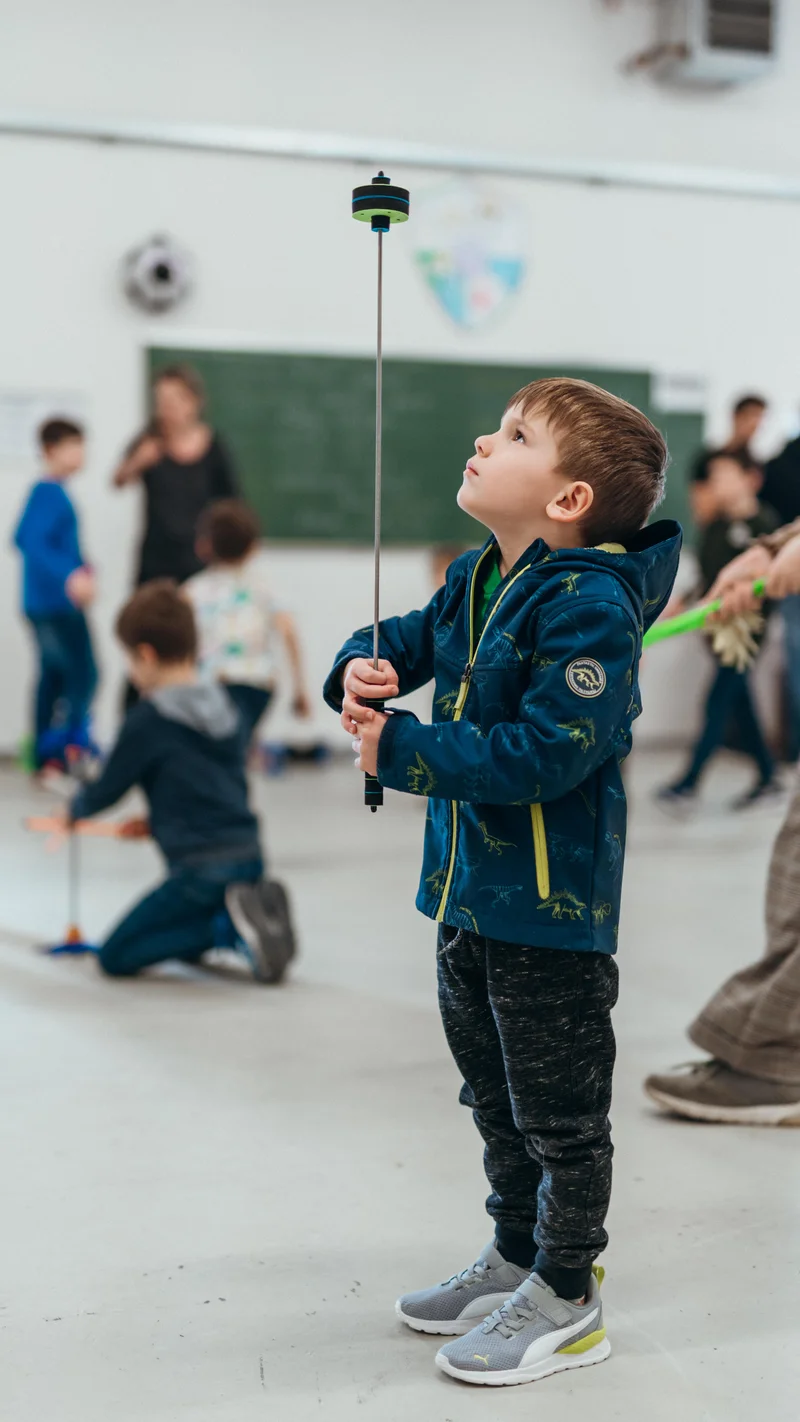 RawmanPictures - Sebastian Schiefermayr | Jonglierworkshop Marchtrenk | Kind spielt mit einem Balancierstab in der Turnhalle. Kinderfotografie, Indoor-Sport, Bewegung.