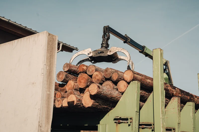 RawmanPictures - Sebastian Schiefermayr | Sägewerk Löberbauer | Effiziente Holzverladung: Kran transportiert Baumstämme für nachhaltige Forstwirtschaft.