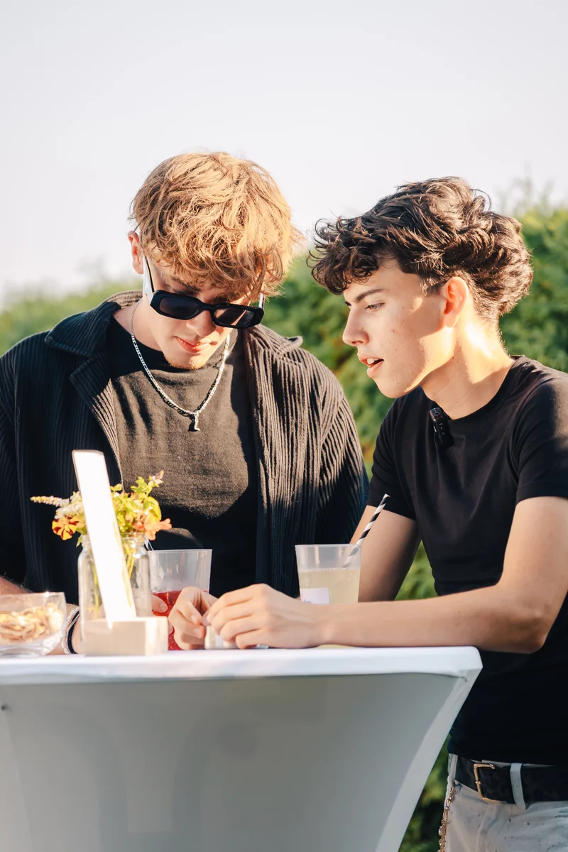 RawmanPictures - Sebastian Schiefermayr | Vality & Friends | Zwei junge Männer im Gespräch an einem Stehtisch, stilvolle Eventfotografie im Freien.