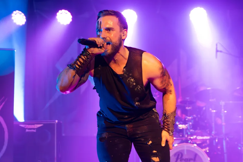 RawmanPictures - Sebastian Schiefermayr | Krampusnacht | Rockkonzert-Fotografie: Energischer Sänger auf der Bühne mit lila Licht und intensiver Performance.