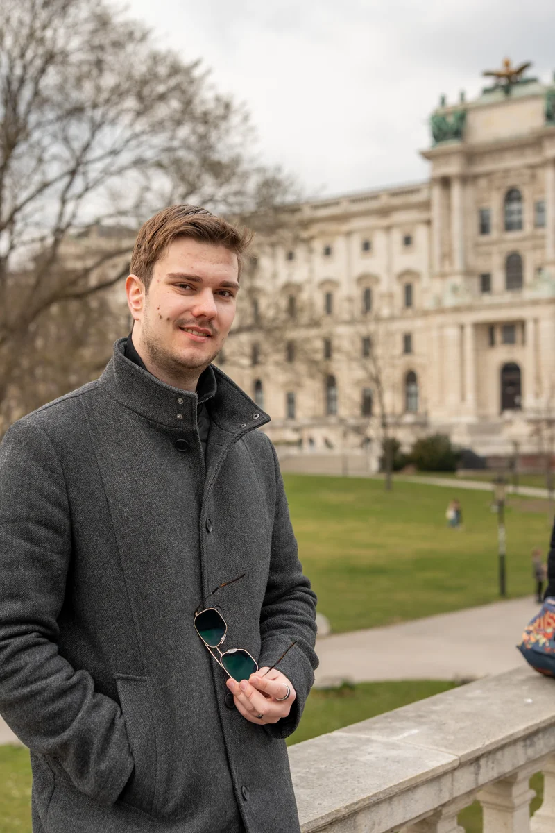 RawmanPictures - Sebastian Schiefermayr | Daytrip Wien | Junger Mann vor historischer Architektur im Park – Porträtfotografie im Freien.