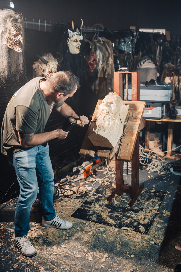 RawmanPictures - Sebastian Schiefermayr | Maskenausstellung | Künstler beim Holzschnitzen, traditionelle Handwerkskunst, kreative Werkstattatmosphäre.