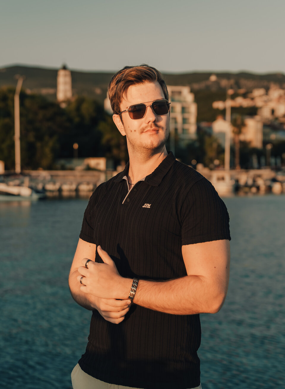 Junger Mann posiert stilvoll vor malerischem Hafen im Abendlicht. Fotografie, Porträt, Sonnenuntergang.