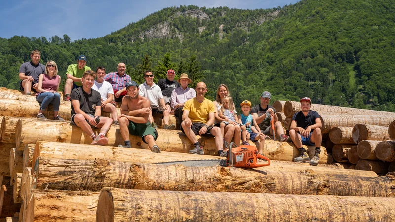 RawmanPictures - Sebastian Schiefermayr | Sägewerk Löberbauer | Gruppe von Holzarbeitern auf Baumstämmen vor Berglandschaft, perfekte Outdoor-Fotografie.