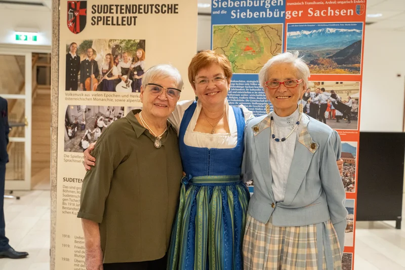 RawmanPictures - Sebastian Schiefermayr | Volkstanzfest | Drei Frauen in traditioneller Tracht vor Infotafeln, kulturelle Fotografie, Eventdokumentation.