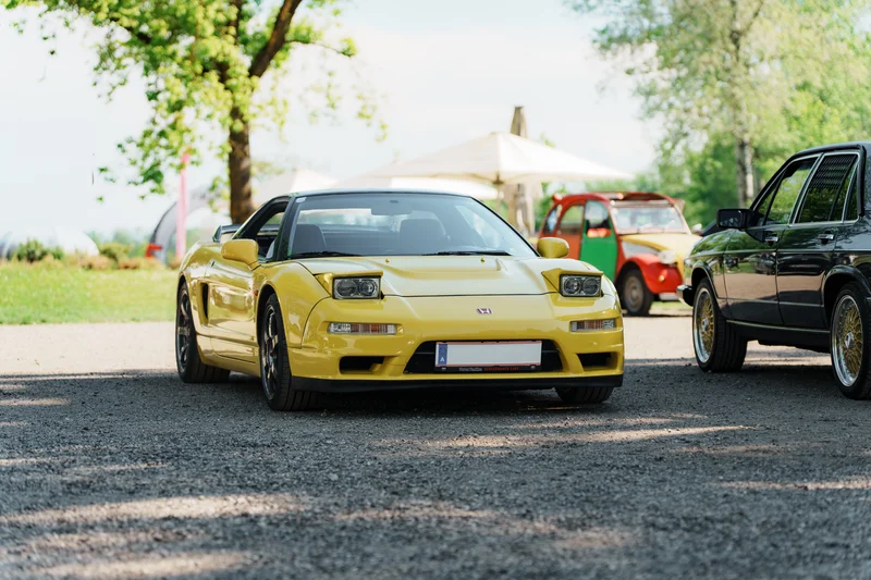 RawmanPictures - Sebastian Schiefermayr | Motortag Feldkirchen | Gelber Sportwagen im Sonnenschein auf Parkplatz, umgeben von Bäumen und Oldtimern.