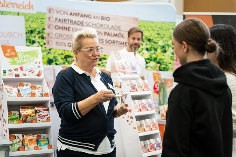 RawmanPictures - Sebastian Schiefermayr | Marke[ding] Wels | Verkaufsstand für Bio-Produkte auf Messe, präsentiert von Expertin. Nachhaltige Lebensmittel.
