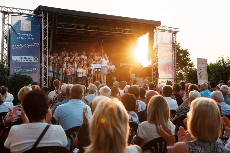 RawmanPictures - Sebastian Schiefermayr | Singkreis-Sundowner  | Outdoor-Konzert bei Sonnenuntergang, Publikum applaudiert, Bühne mit Chor in idyllischer Abendstimmung.