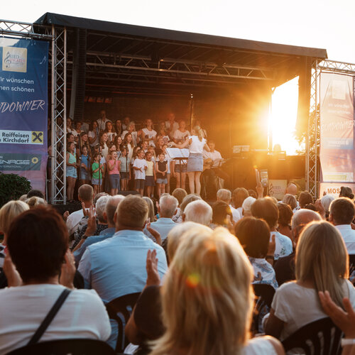 RawmanPictures - Sebastian Schiefermayr | Singkreis-Sundowner  | Outdoor-Konzert bei Sonnenuntergang, Publikum applaudiert, Bühne mit Chor in idyllischer Abendstimmung.