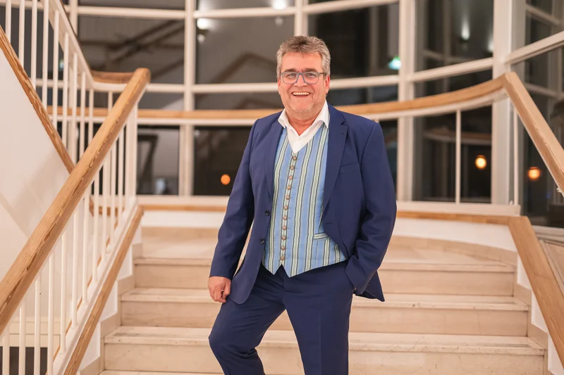 RawmanPictures - Sebastian Schiefermayr | Volkstanzfest | Eleganter Herr im Anzug auf Treppe, Innenporträt, professionelle Fotografie.