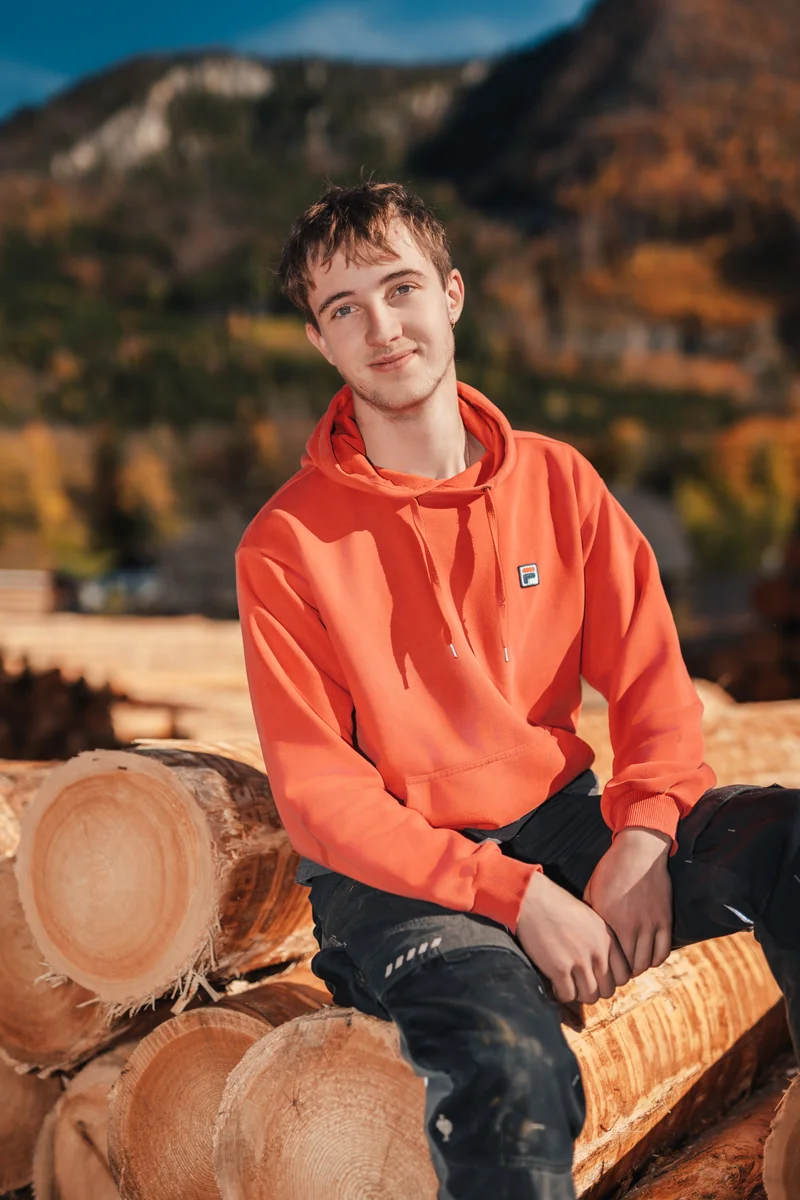 RawmanPictures - Sebastian Schiefermayr | Sägewerk Löberbauer | Junger Mann im Freien mit Holzstämmen und Bergen, Herbstlandschaft, stimmungsvolles Portraitfoto.