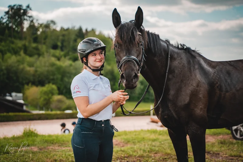 RawmanPictures - Sebastian Schiefermayr | Vielseitigkeits­turnier | Reiterin mit Helm und Pferd auf Wiese beim Fotoshooting im Freien.