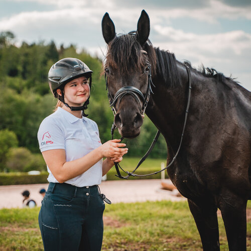 RawmanPictures - Sebastian Schiefermayr | Vielseitigkeits­turnier | Reiterin mit Helm und Pferd auf Wiese beim Fotoshooting im Freien.