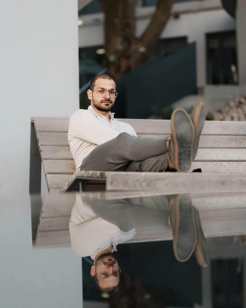 RawmanPictures - Sebastian Schiefermayr | Fotowalk Burhan | Mann auf einer Bank, reflektiert auf Glasoberfläche. Moderne Porträtfotografie.