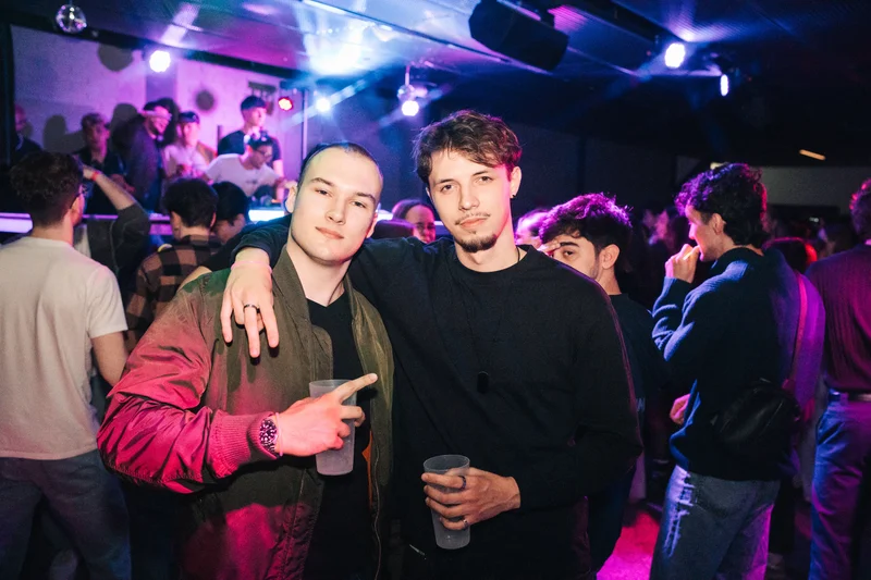 RawmanPictures - Sebastian Schiefermayr | JKU Mensafest | Party-Nacht: Zwei Freunde posieren im Club bei lebhafter Atmosphäre und bunter Beleuchtung.