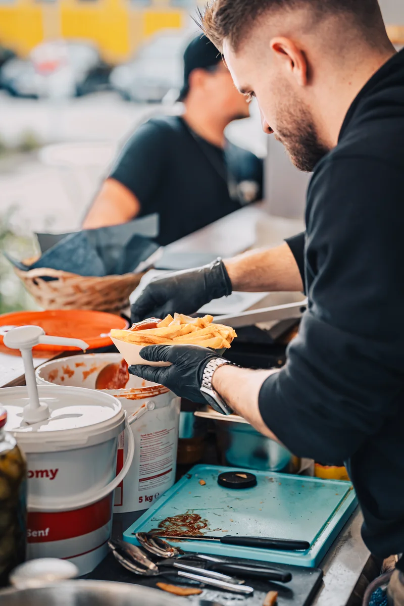 RawmanPictures - Sebastian Schiefermayr | Maskenausstellung | Ein Streetfood-Stand mit frisch zubereiteten Pommes und engagiertem Personal.