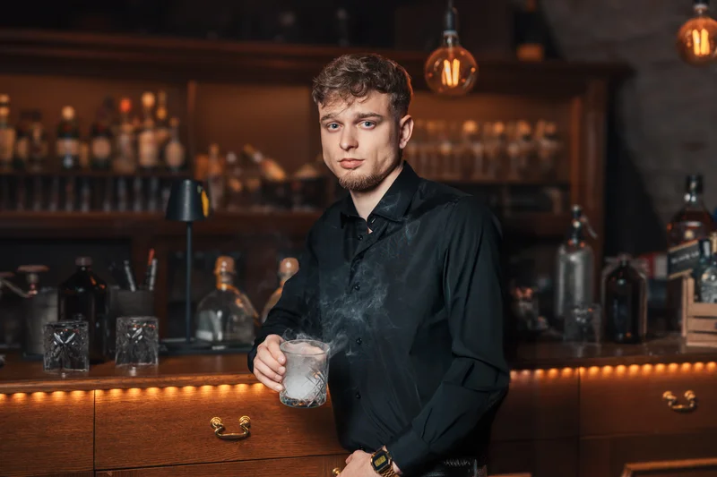 RawmanPictures - Sebastian Schiefermayr | Portraitshooting Kevin F. | Mann an Bar mit Cocktail in stilvoller Beleuchtung für Bar- und Eventfotografie.