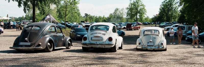 RawmanPictures - Sebastian Schiefermayr | Motortag Feldkirchen | Klassisches Autotreffen im Freien: Drei Retro-VWs, sonniger Tag, voller Parkplatz.