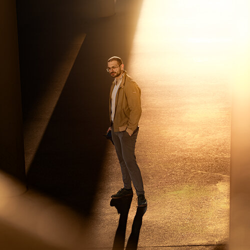 RawmanPictures - Sebastian Schiefermayr | Fotowalk Burhan | Mann im Sonnenlicht unter einer Brücke, atmosphärische Urban Photography, kreative Beleuchtung.