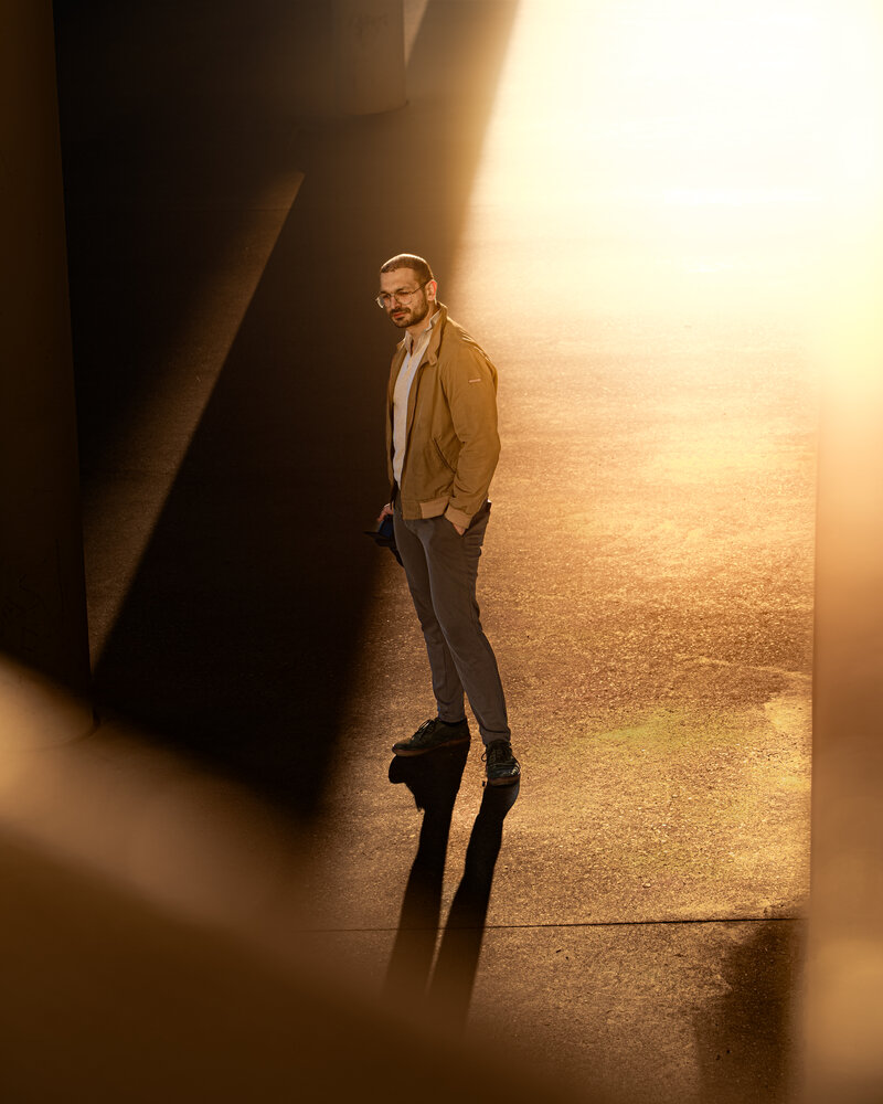 RawmanPictures - Sebastian Schiefermayr | Fotowalk Burhan | Mann im Sonnenlicht unter einer Brücke, atmosphärische Urban Photography, kreative Beleuchtung.