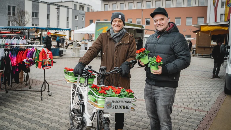 RawmanPictures - Sebastian Schiefermayr | Valentinsaktion Marchtrenk | Zwei Männer mit Blumen auf Markt, fröhlich, urbana Fotografie, Lifestyle, Stadtleben.