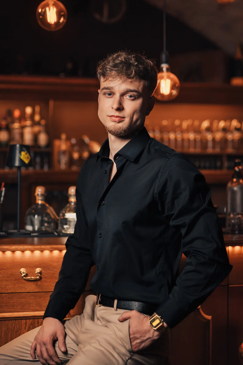 RawmanPictures - Sebastian Schiefermayr | Portraitshooting Kevin F. | Barportrait eines Mannes in eleganter Kleidung vor einer stilvollen Bar-Atmosphäre.