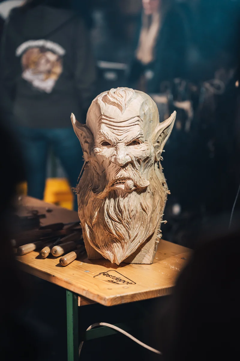 RawmanPictures - Sebastian Schiefermayr | Maskenausstellung | Holzschnitzerei-Workshop: Detaillierte Skulptur eines Fabelwesens auf Arbeitstisch.